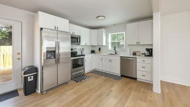 Una cocina moderna con armarios blancos, electrodomésticos de acero inoxidable y piso de madera.
