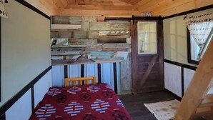 Una habitación pequeña y acogedora con techo y paredes de madera, una cama con colcha estampada, una silla de madera y una mesita.