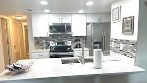 A modern kitchen with white cabinets, stainless steel appliances, a central island with a sink, and a coffee machine. - Grand Family 3BD Condo Apartment Near Disney Parks 5 (Kissimmee)