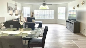 A spacious living room with a dining area, a ceiling fan, and a television on a cabinet. - Grand Family 3BD Condo Apartment Near Disney Parks 5 (Kissimmee)