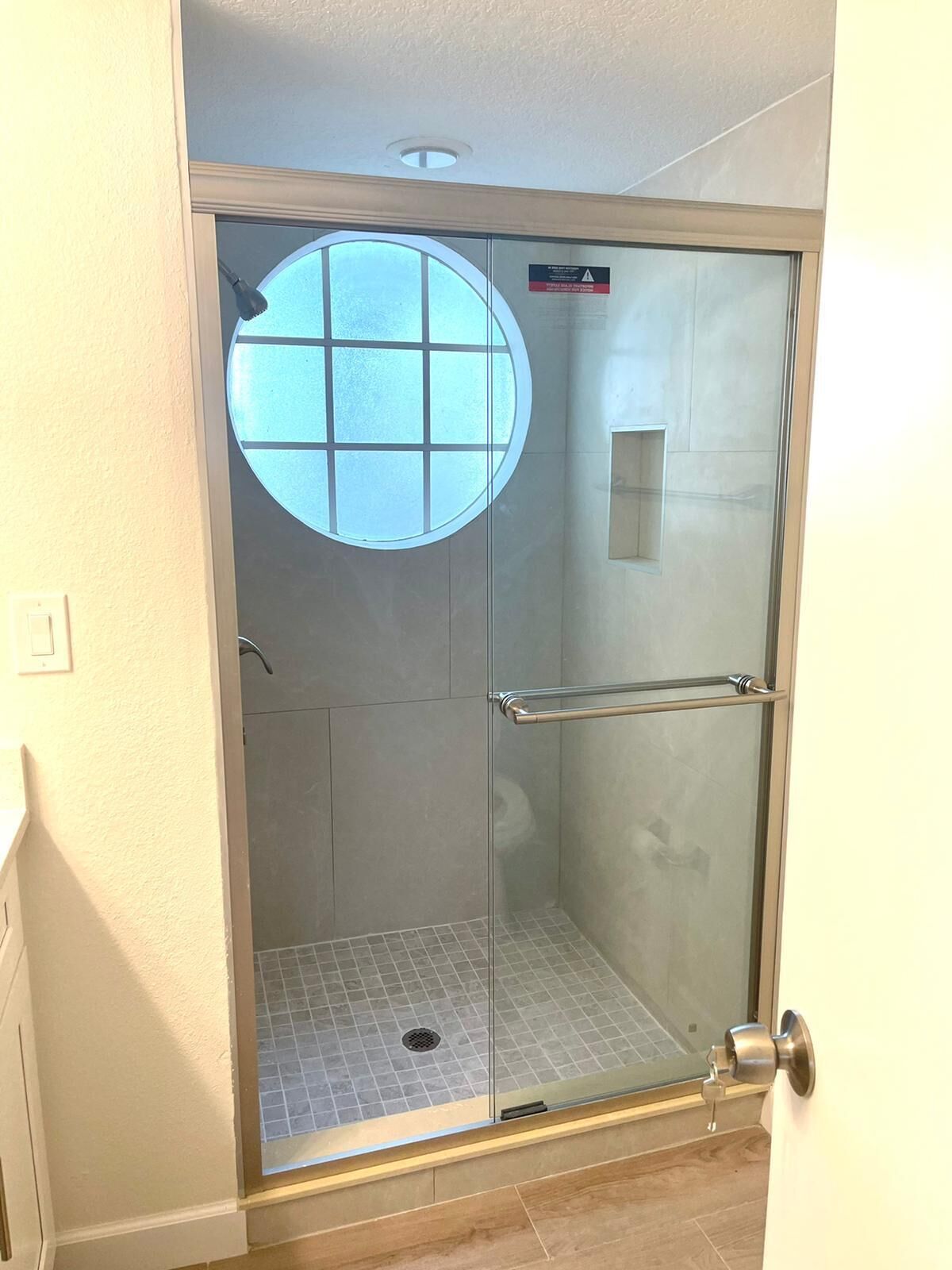 A glass-enclosed shower with a circular window, a towel rack, and a door with a key lock.