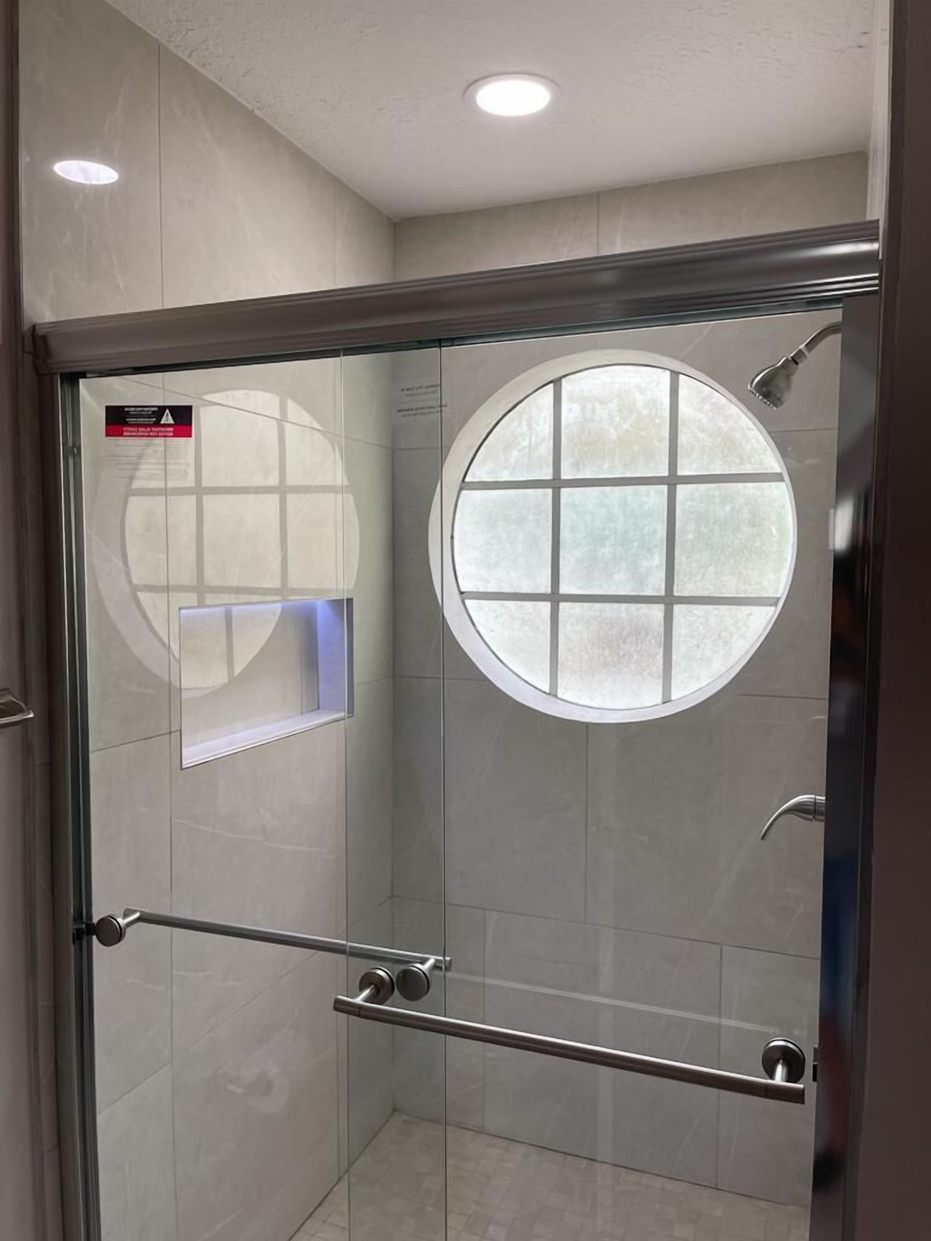 Une douche moderne dotée d’une porte en verre, d’une fenêtre ronde et d’une barre d’appui.