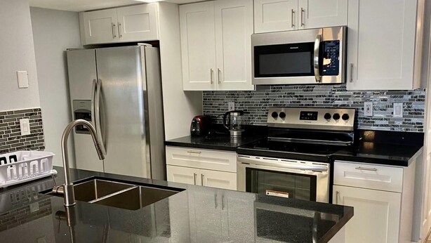 A modern kitchen with white cabinets, stainless steel appliances, and a black granite countertop.