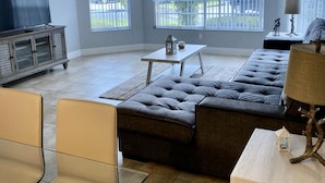 A spacious living room with a sectional sofa, a television on a cabinet, and a ceiling fan.