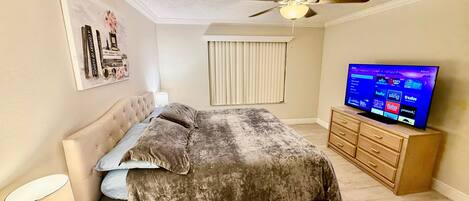 A bedroom with a bed, a ceiling fan, a television, and a dresser.