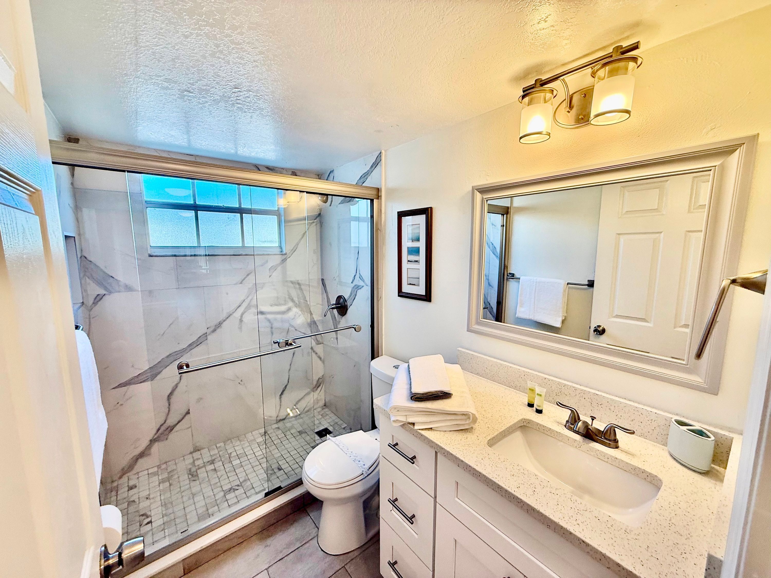 A bathroom with a glass-enclosed shower, a toilet, a sink, and a large mirror.