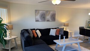 A modern living room with a sectional sofa, a coffee table, and a ceiling fan. - Grand Family Superior 3BD Condo Near Disney 7 (Kissimmee)