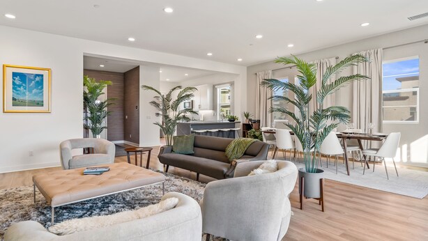 A modern living room with a sofa, armchairs, and a coffee table. There is a dining area with a table and chairs. The room has large windows and potted plants. - Brand new luxury home near Tahquitz Creek Golf Course with mountain views! (Palm Springs)