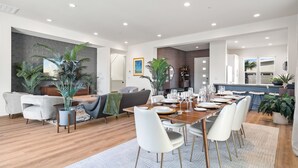 A spacious modern living room with a dining area, featuring a large wooden table set for six, white chairs, and a grey sofa. - Brand new luxury home near Tahquitz Creek Golf Course with mountain views! (Palm Springs)
