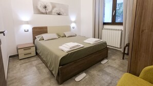 Et pænt og ryddeligt soveværelse med seng, sengeborde, et vindue med gardiner og en radiator.