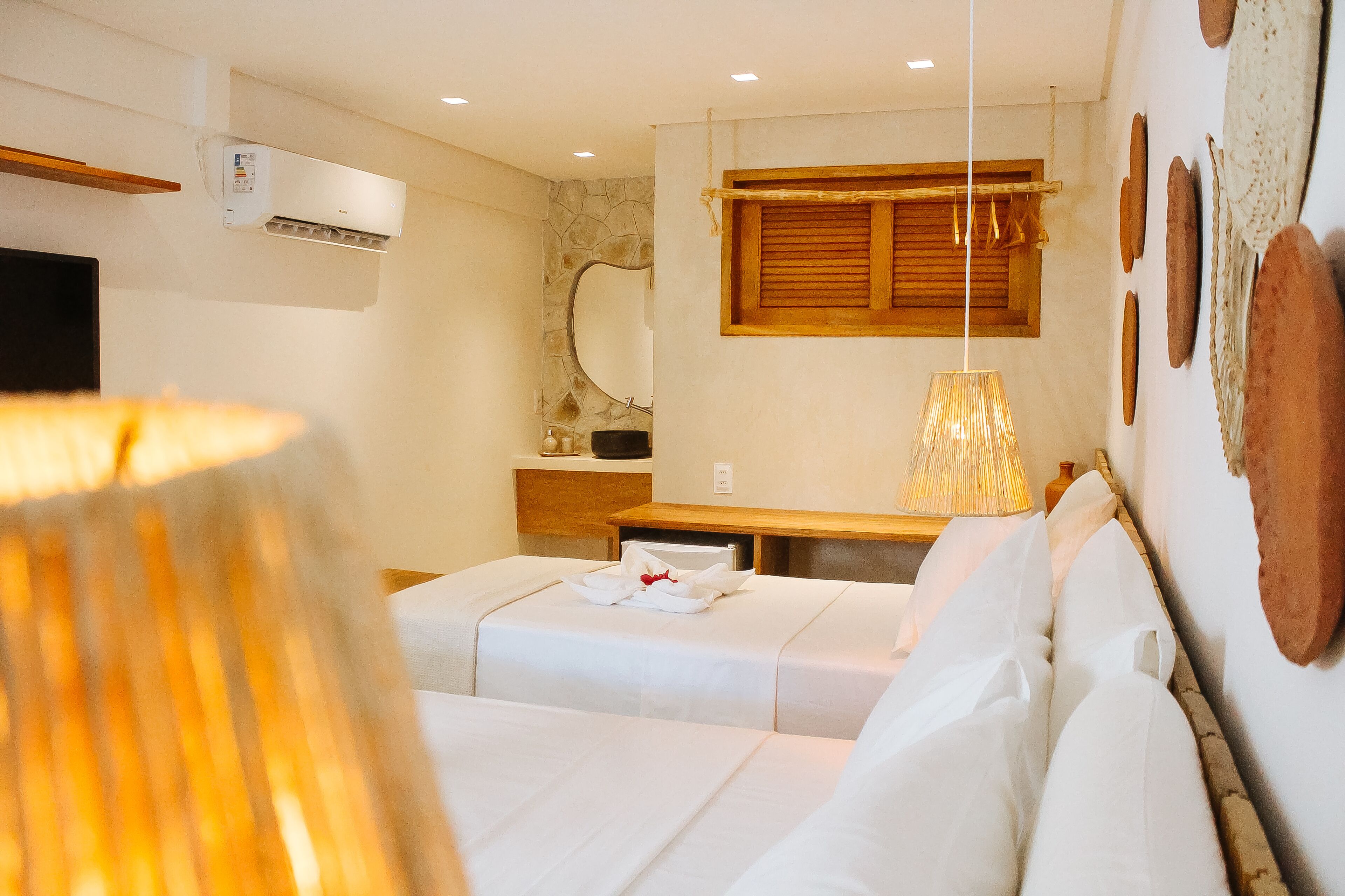 A hotel room with a bed, a bedside table, a lamp, a mirror, and a wall-mounted air conditioner.