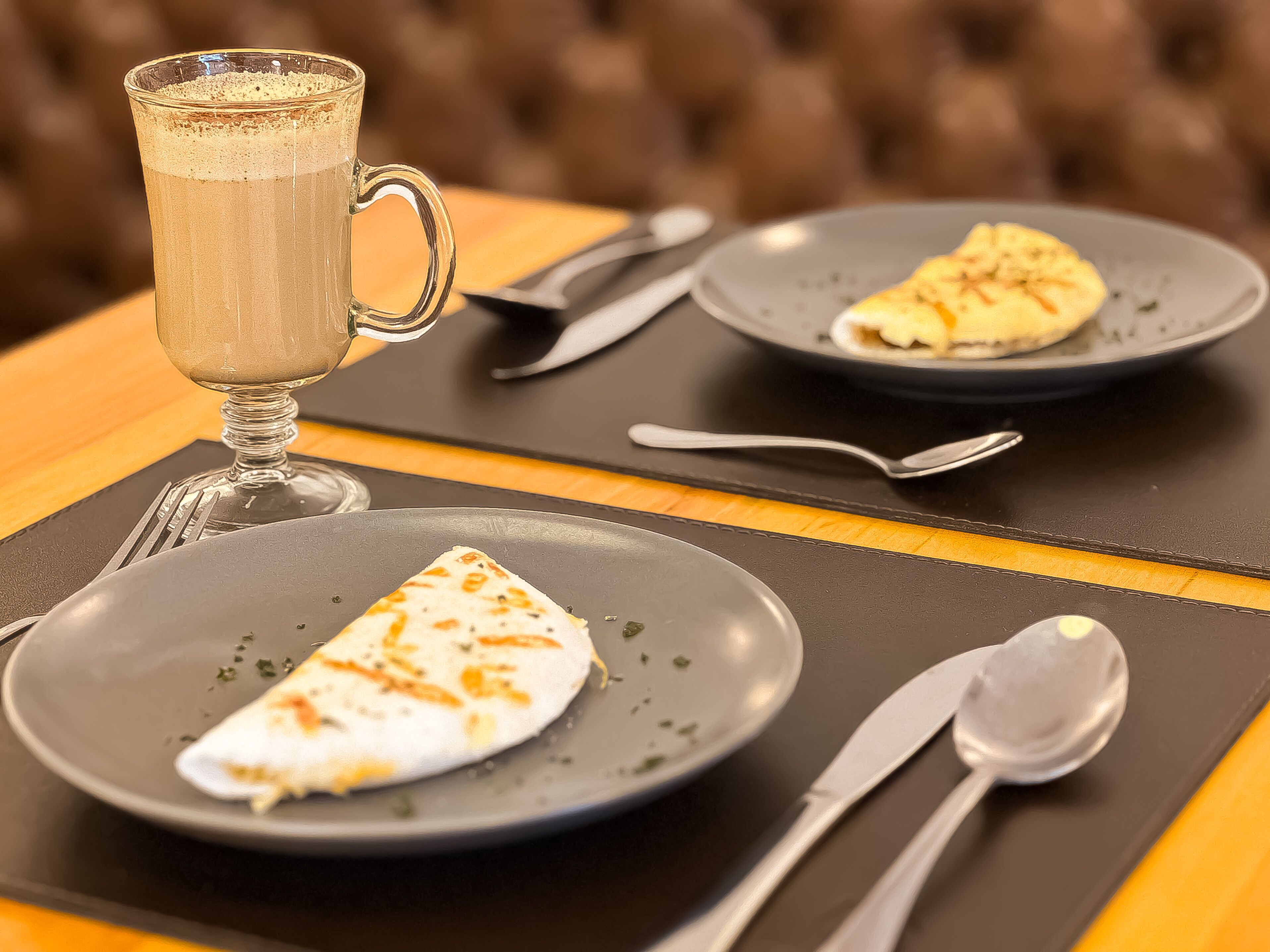 A dining table with a glass mug, plates with food, cutlery, and a napkin.