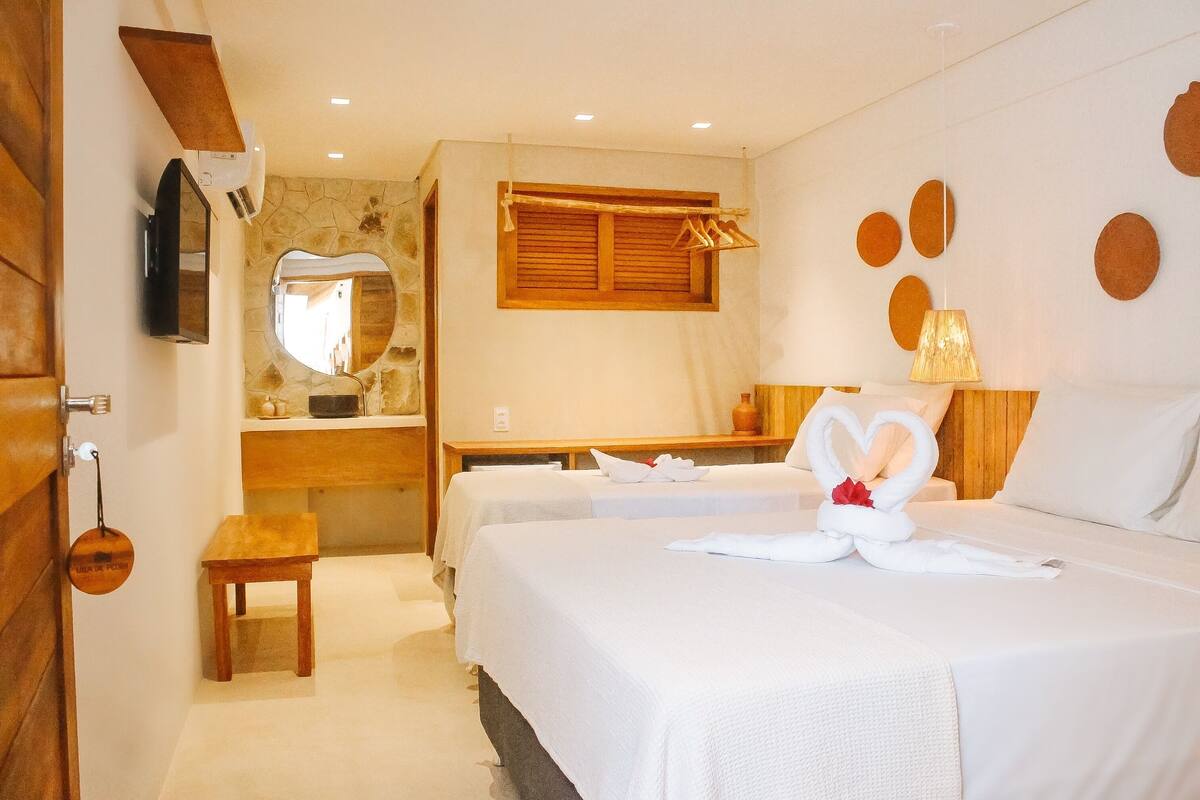 Une chambre d’hôtel avec deux lits, un bureau en bois, un miroir et un téléviseur fixé au mur.