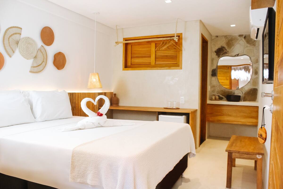 Une chambre d’hôtel avec un lit, un bureau, un miroir et un petit tabouret en bois.