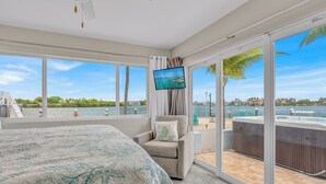 Une chambre avec un grand lit, une télévision et une vue sur l’eau grâce à de grandes fenêtres.