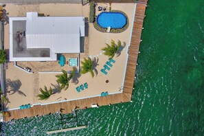 Eine Vogelperspektive zeigt ein Resort mit Schwimmbad, Wellnessbereich und Strand, inklusive Liegestühlen.