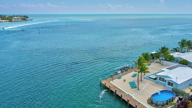Une propriété située en bord de mer, dotée d’un quai en bois, d’une piscine et d’un espace de plage avec des chaises longues.