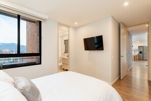 A modern hotel room with a large bed, a TV mounted on the wall, and a view of the city through a window. - Tasteful flat with amazing view in El Poblado wtih pool and gym (Medellín)