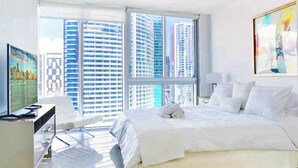 A modern hotel room with a large bed, a desk, a chair, and a TV. - Icon Brickell Condo - We Host (Miami)