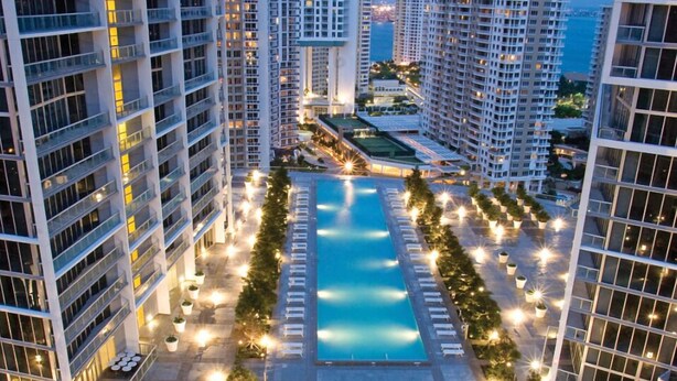 A high-rise hotel with multiple floors, a central swimming pool, and a well-lit outdoor area with lights and greenery. - Icon Brickell Condo - We Host (Miami)