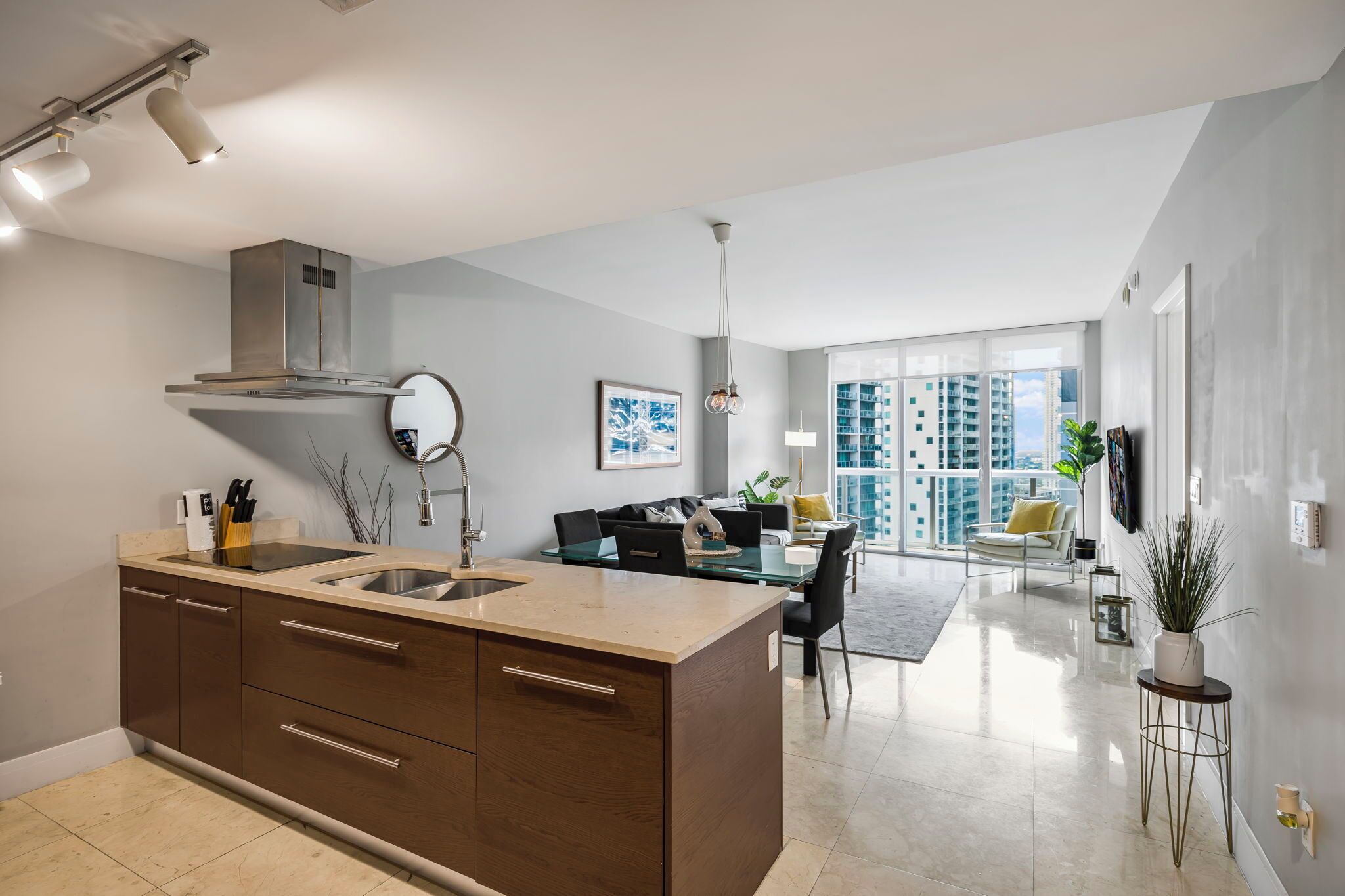 A modern kitchen with a central island, a dining area with a glass table, and a view of high-rise buildings.