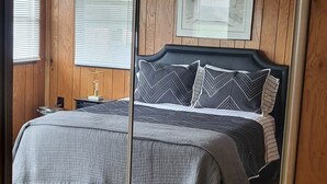 Een slaapkamer met een bed, houten paneelwanden, een ingelijst kunstwerk en een raam met jaloezieën.