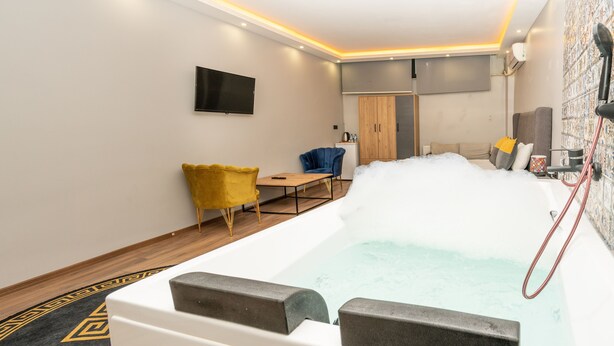 Un baño moderno con una bañera grande, piso de madera, una silla amarilla y una silla azul.