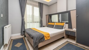 Una habitación de hotel moderna con una cama grande, una mesita de noche con un teléfono, un armario y una ventana con cortinas.