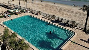 Zona de piscina amb aigua cristal·lina blava, envoltada de gandules i palmeres, amb vista a una platja sorrenca i l'oceà.