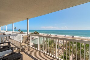 Un balcon avec vue sur la plage, des balustrades blanches et des sièges d’extérieur.