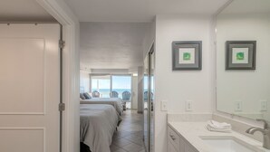 Habitació d'hotel amb una finestra gran, un bany amb un lavabo i un mirall, i dos llits amb roba de llit gris.