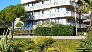 A multi-story building with balconies, a green lawn, and palm trees. - Cozy Apartment Facing the sea (San Michele al Tagliamento)