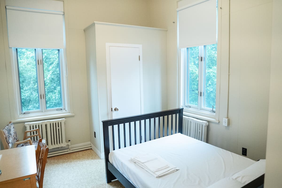 Un dormitorio con cama, una silla, una mesa y un armario.