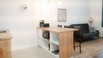 A modern kitchen with a wooden island, white cabinets, and a microwave. There is a sofa and a lamp in the living area.