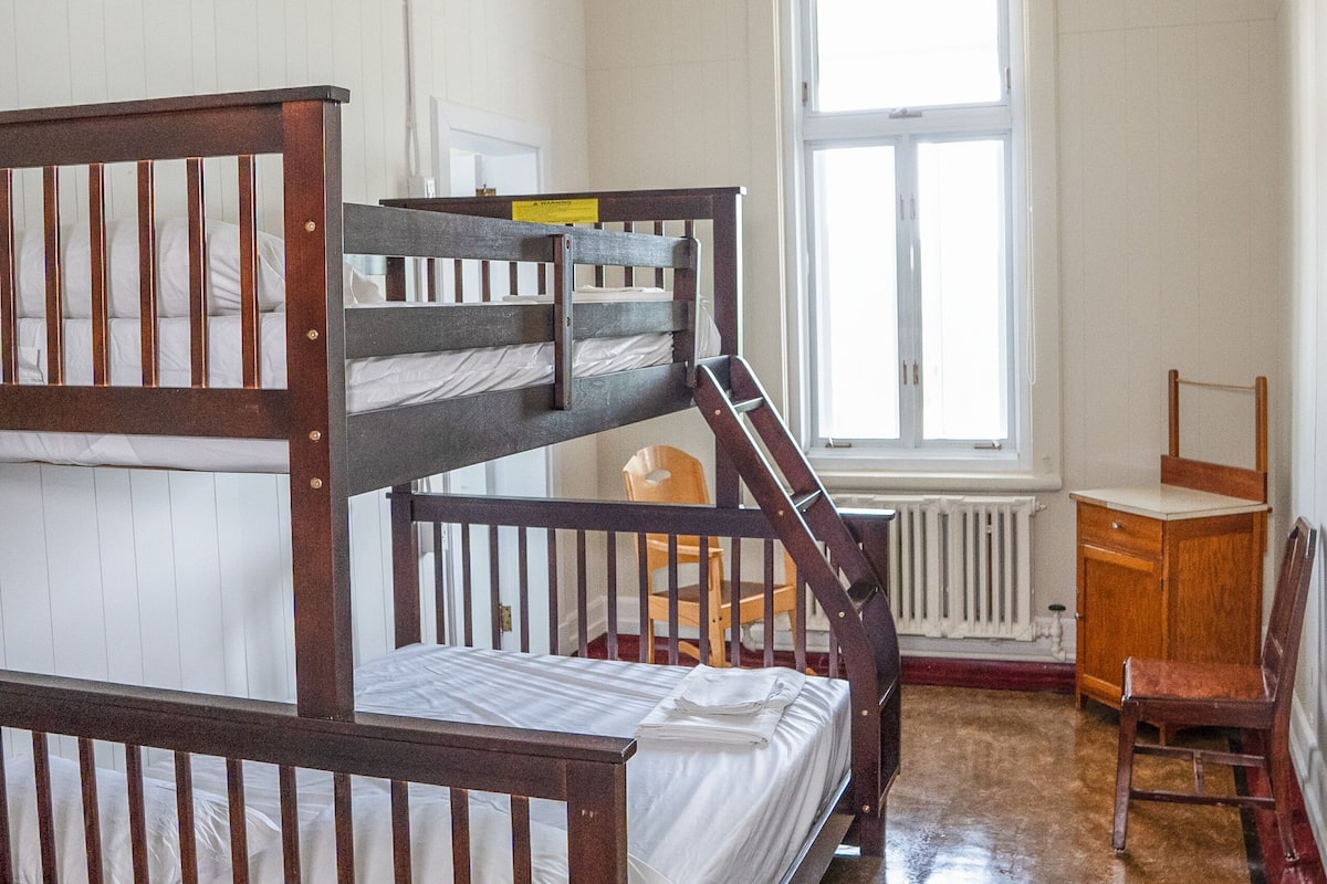 Dormitorio con literas, un radiador, una ventana y un escritorio.