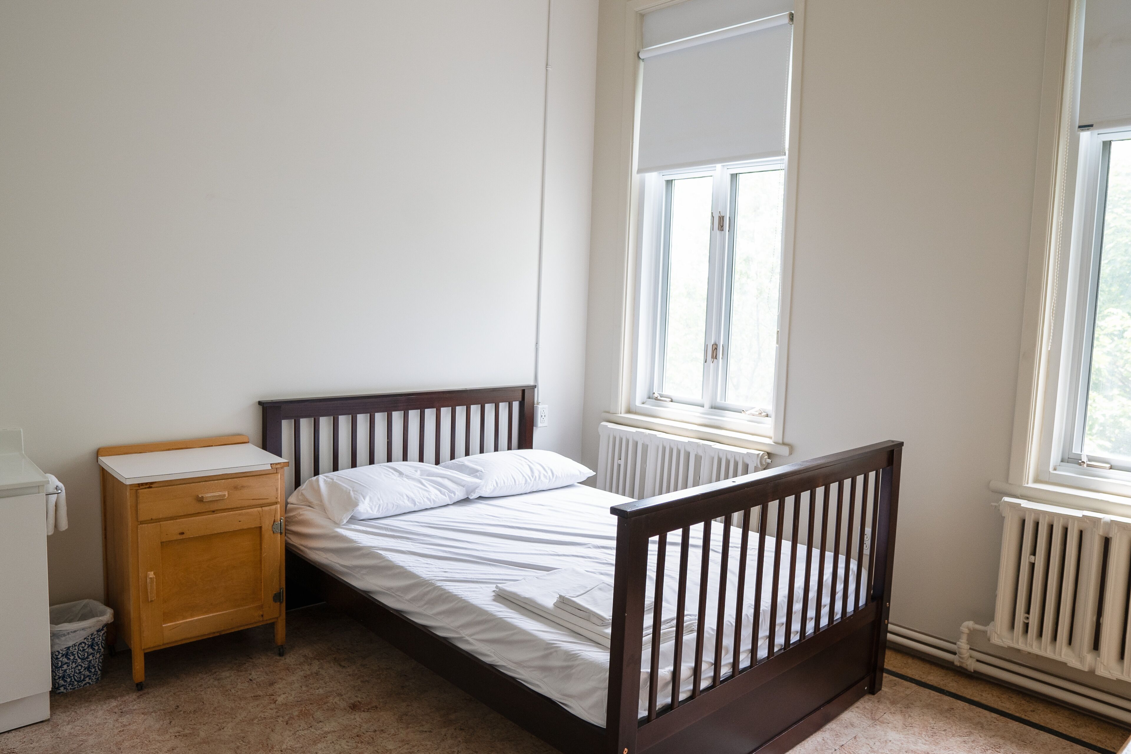 Een slaapkamer met een enkel bed, een houten nachtkastje, een radiator en een raam.