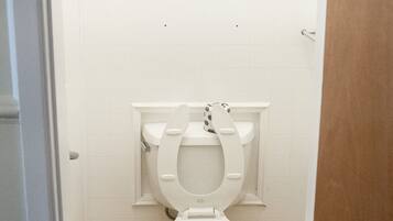 A small, white toilet in a narrow bathroom with white tiled walls and a beige floor.