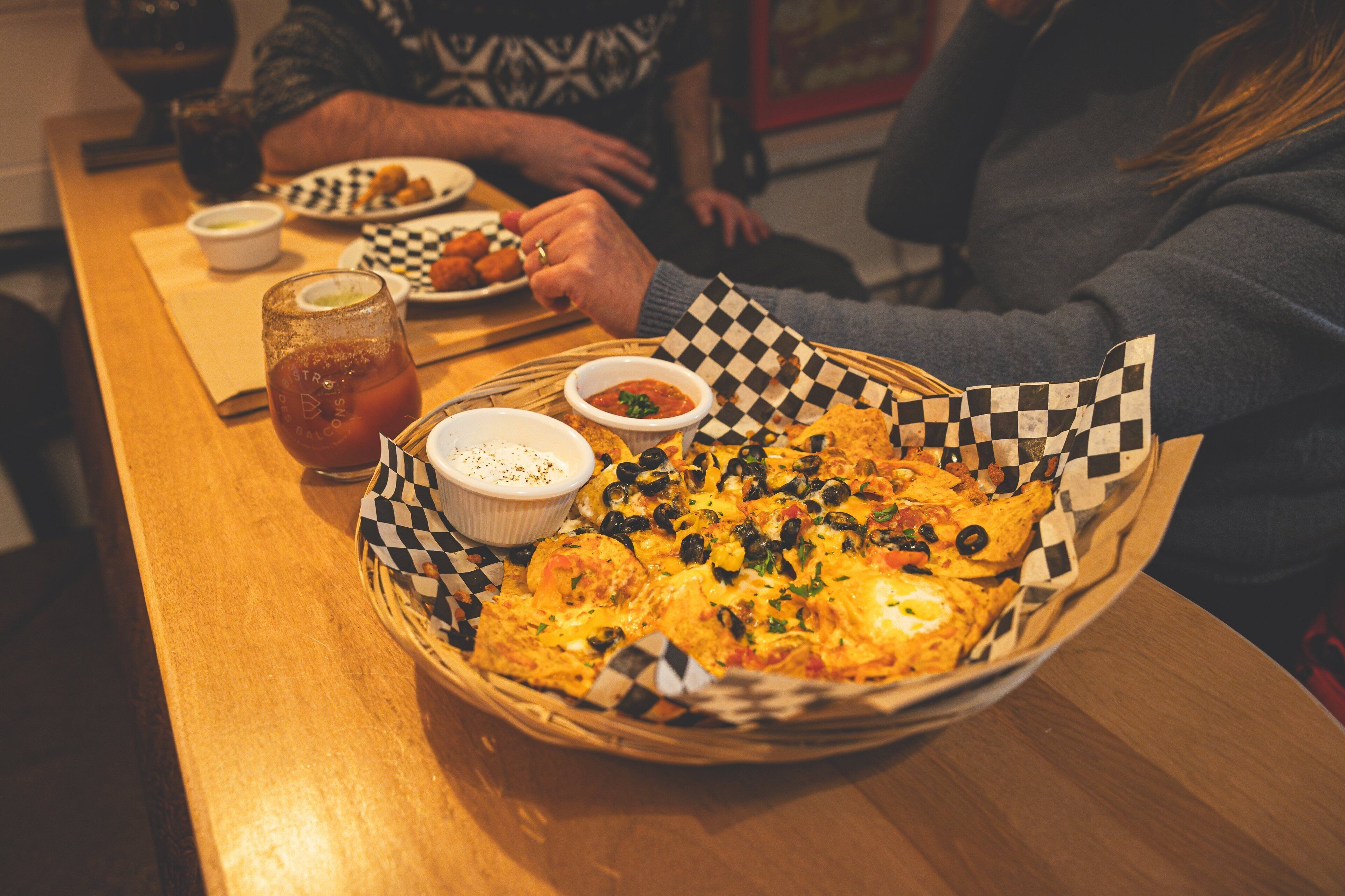 A table with a basket containing a dish, a glass of a beverage, and two small bowls of sauce.
