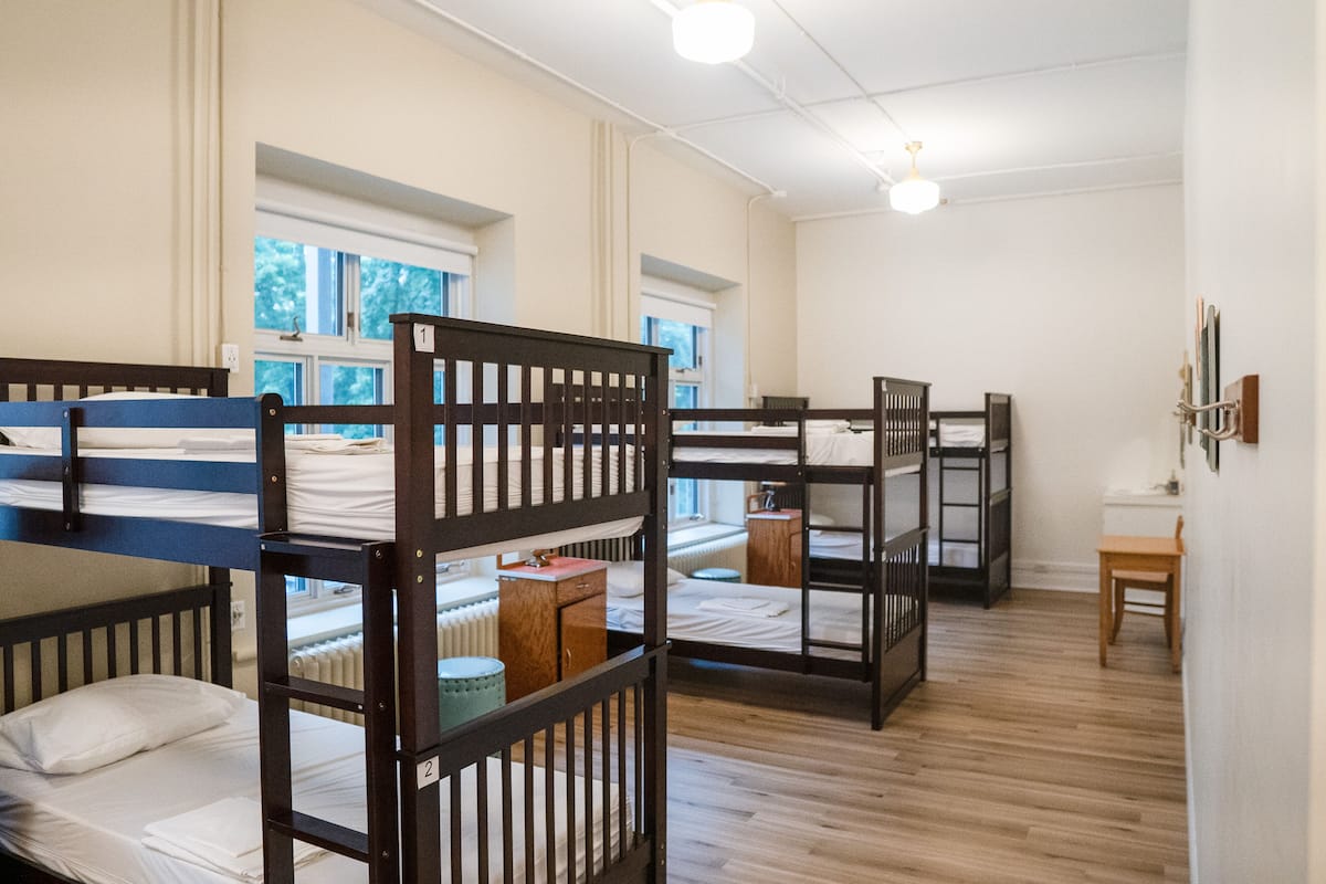 Un dormitorio con literas, piso de madera y una ventana que da a árboles.
