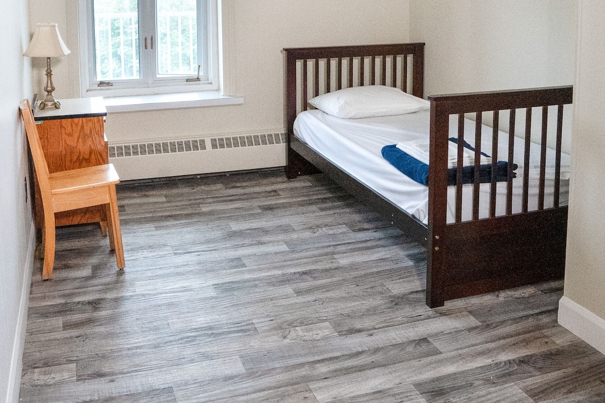 Una habitación pequeña y limpia con una cama individual, un escritorio y una ventana.