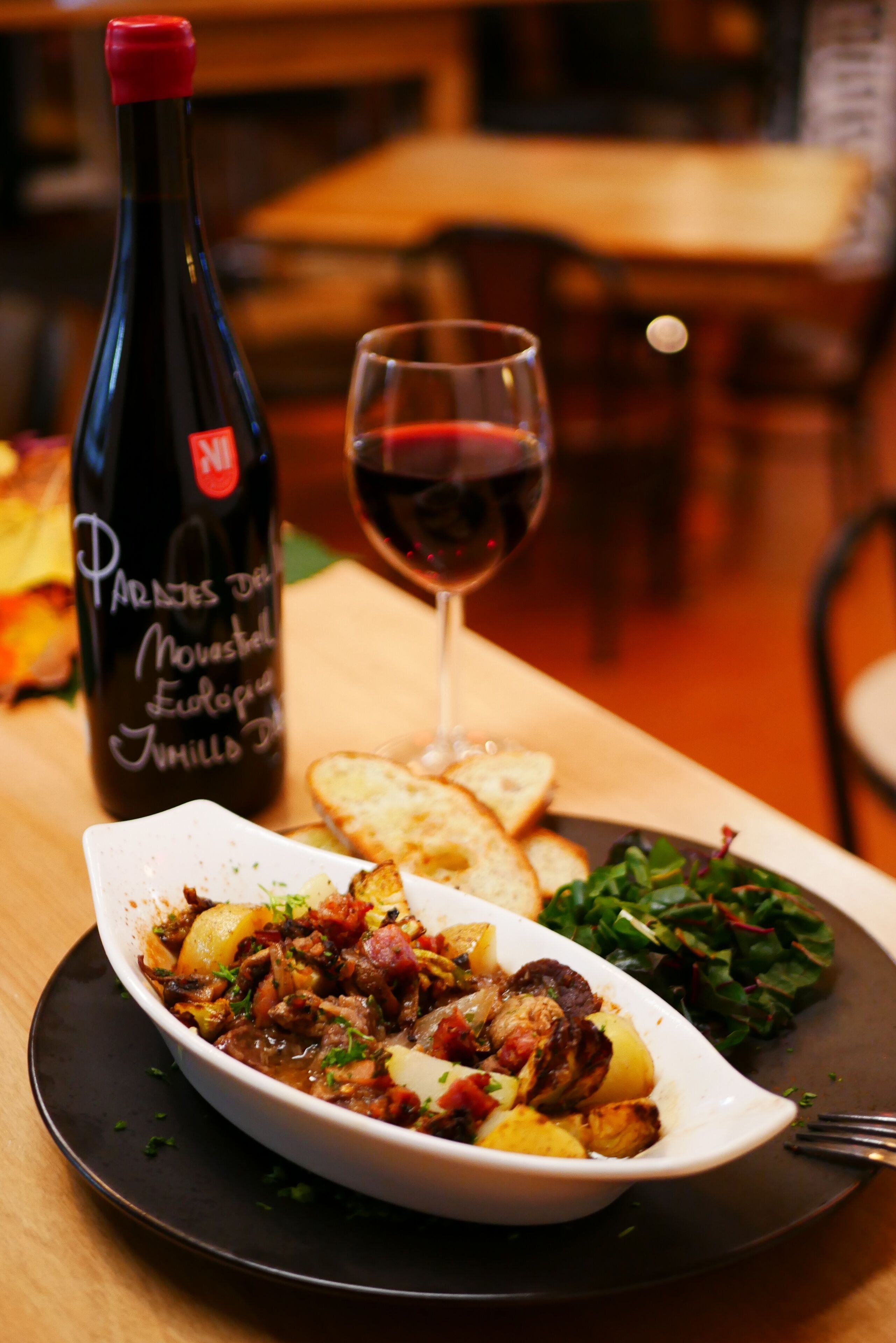 A dining table with a plate of food, a bottle of wine, and a glass of red wine.
