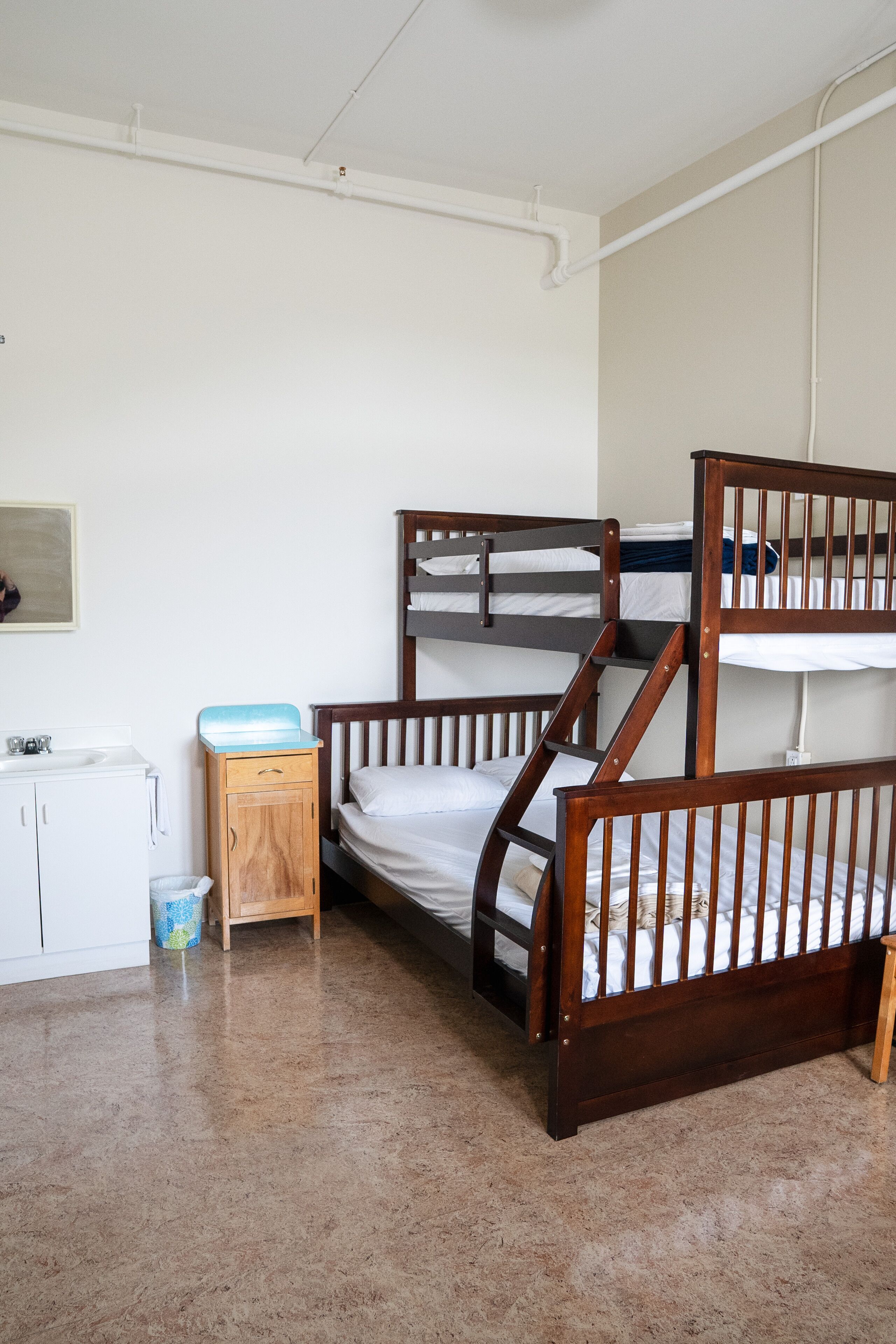 A bunk bed room with a wooden floor, a small wooden cabinet, and a white sink.