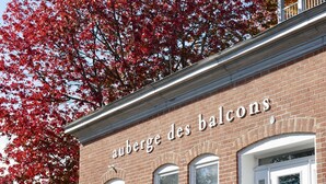 Rakennuksessa on kyltti, jossa lukee ”Auberge des Balcons”, ja portaikko johtaa sisäänkäyntiin.