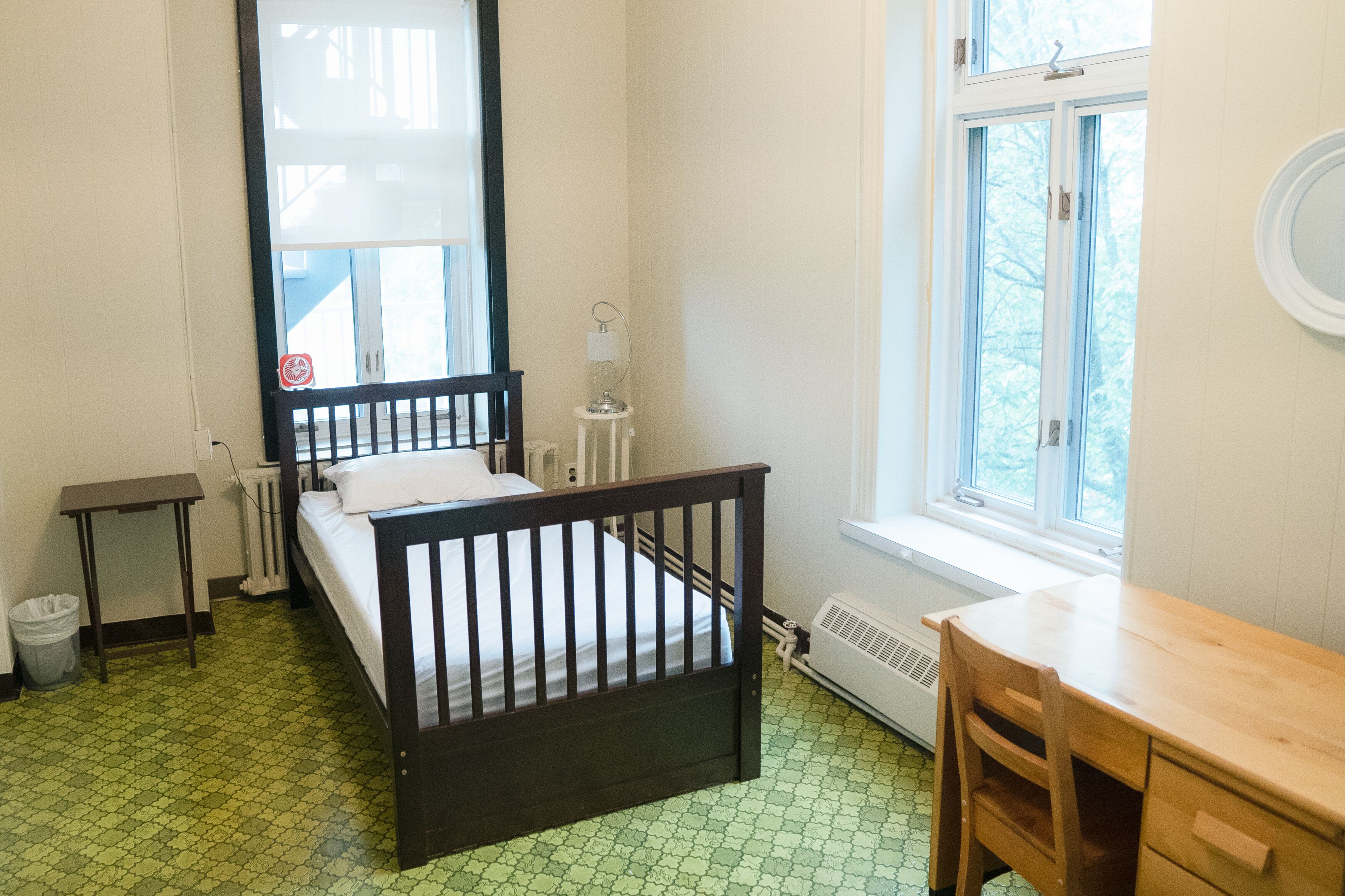 A room with a bed, a desk, a chair, a radiator, and a window.