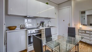 Une cuisine moderne avec des meubles blancs, une table à manger en verre et une chaise noire.