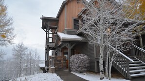 A two-story wooden building with a stone foundation, a covered porch, and a staircase leading to the second floor.