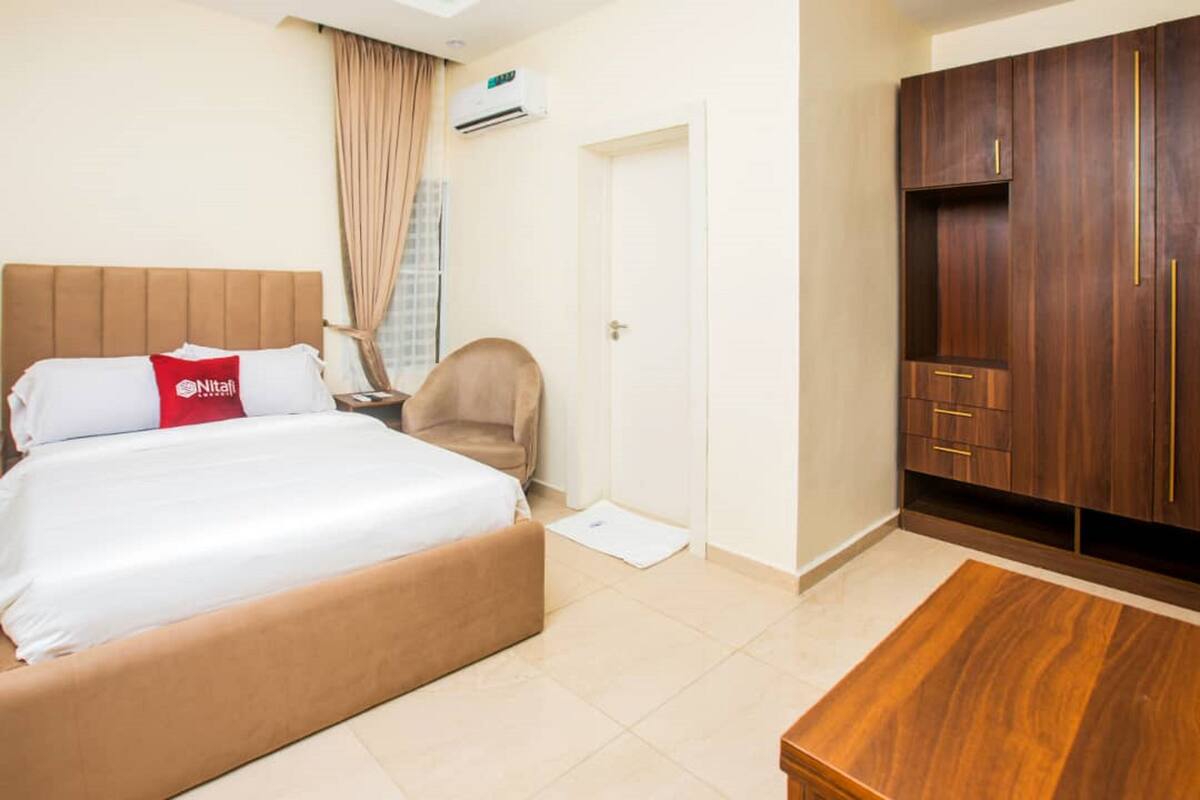 Una habitación de hotel con una cama, una silla, un armario de madera y una mesita.