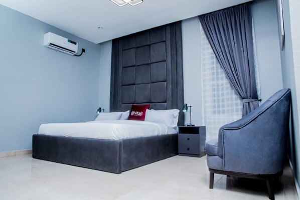 A modern bedroom with a bed, a nightstand, a chair, and a large window with curtains.