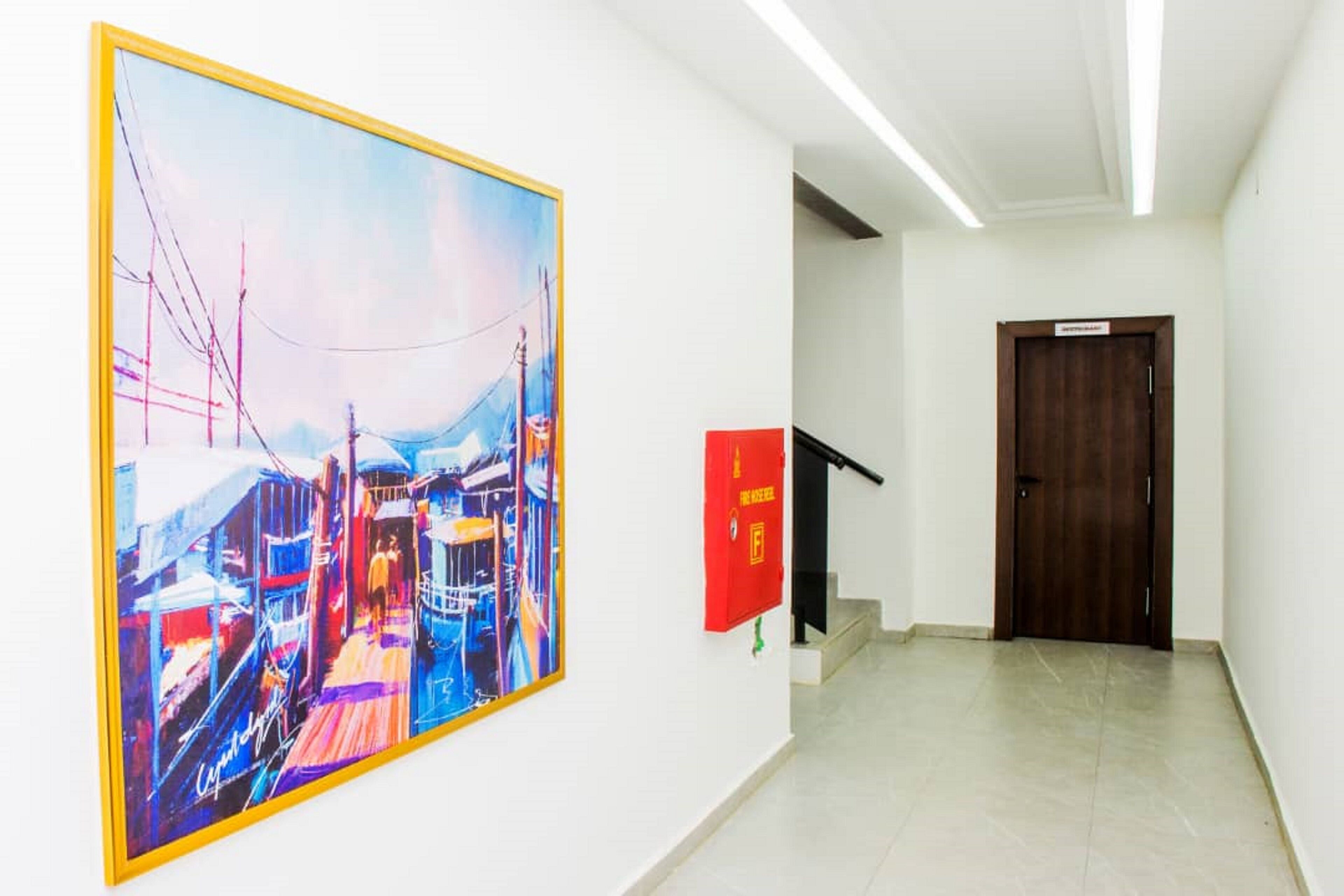A hallway with a large colorful painting, a red emergency box, and a wooden door.