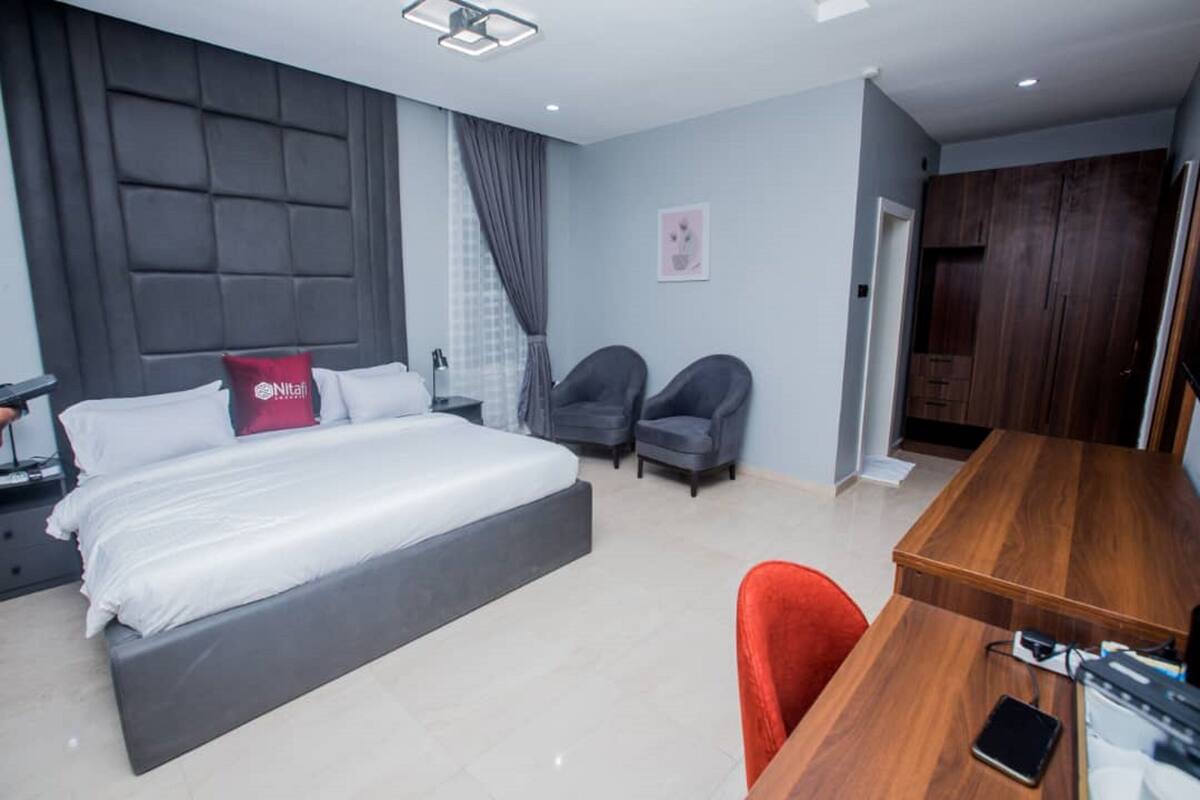 Un dormitorio moderno con una cama grande, dos sillones, un escritorio de madera y un armario.